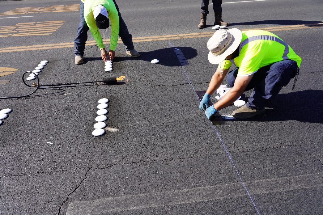 Workers in high-visibility vests installing reflective dots on the roadway